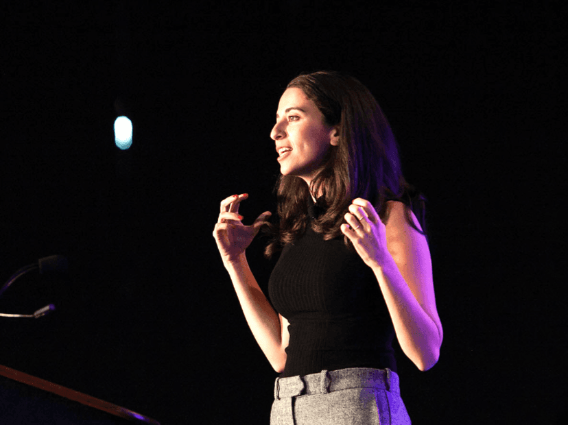 A speaker presenting on stage at a Net Impact event